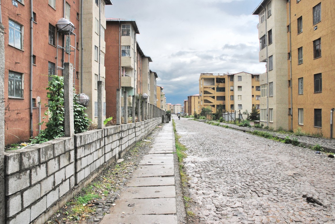 An empty cobblestone street in Addis Ababa on an overcast day. The street is lined with multi-story housing units.